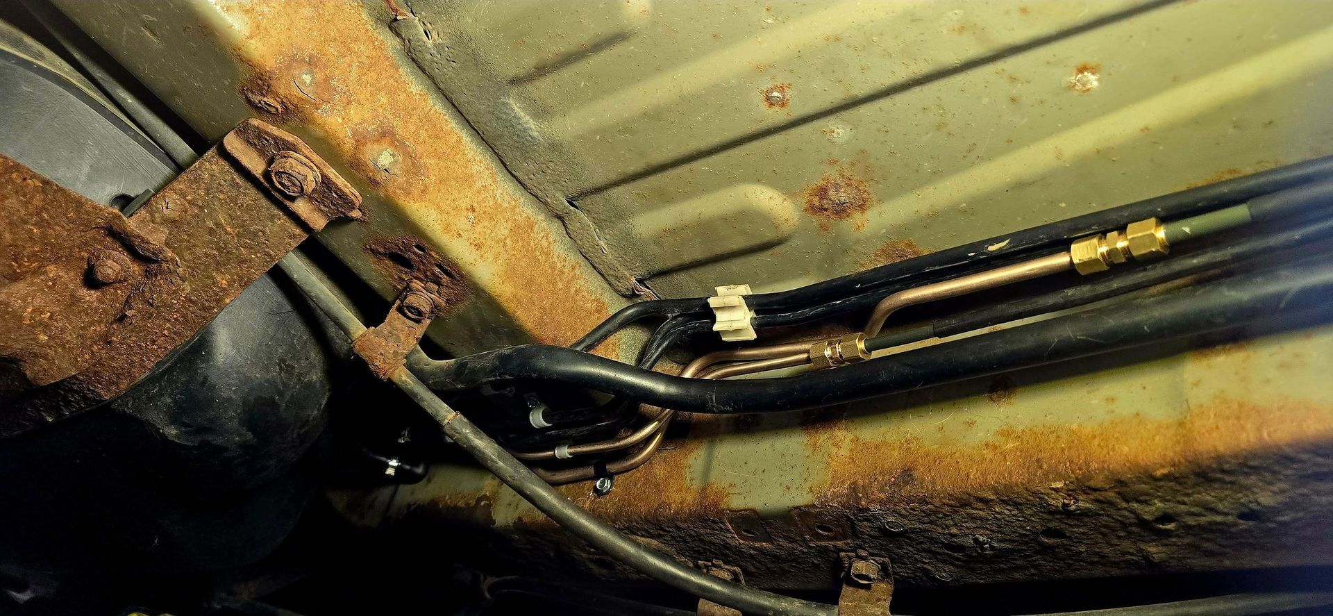 Close-up of a rusty car undercarriage with pipes and metal panels coated in grime.