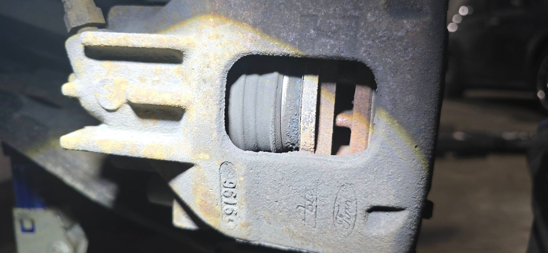 Close-up of a car brake caliper with exposed brake pad and rotor, dusty metal surface.
