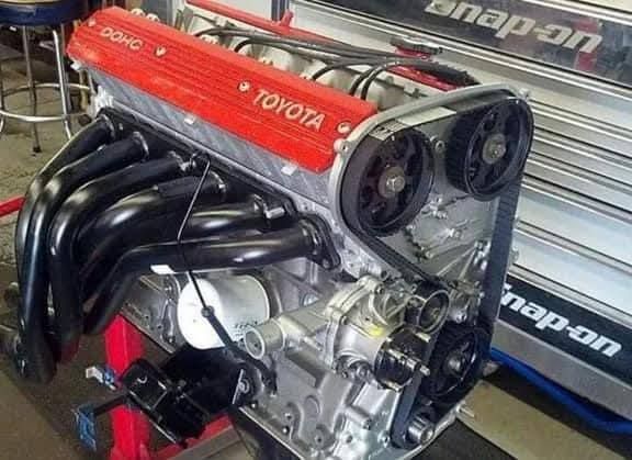 Toyota V8 engine with red valve cover and black headers on a workshop bench