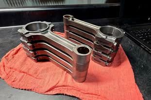 Metal engine rocker arms resting on a red cloth in a workshop.
