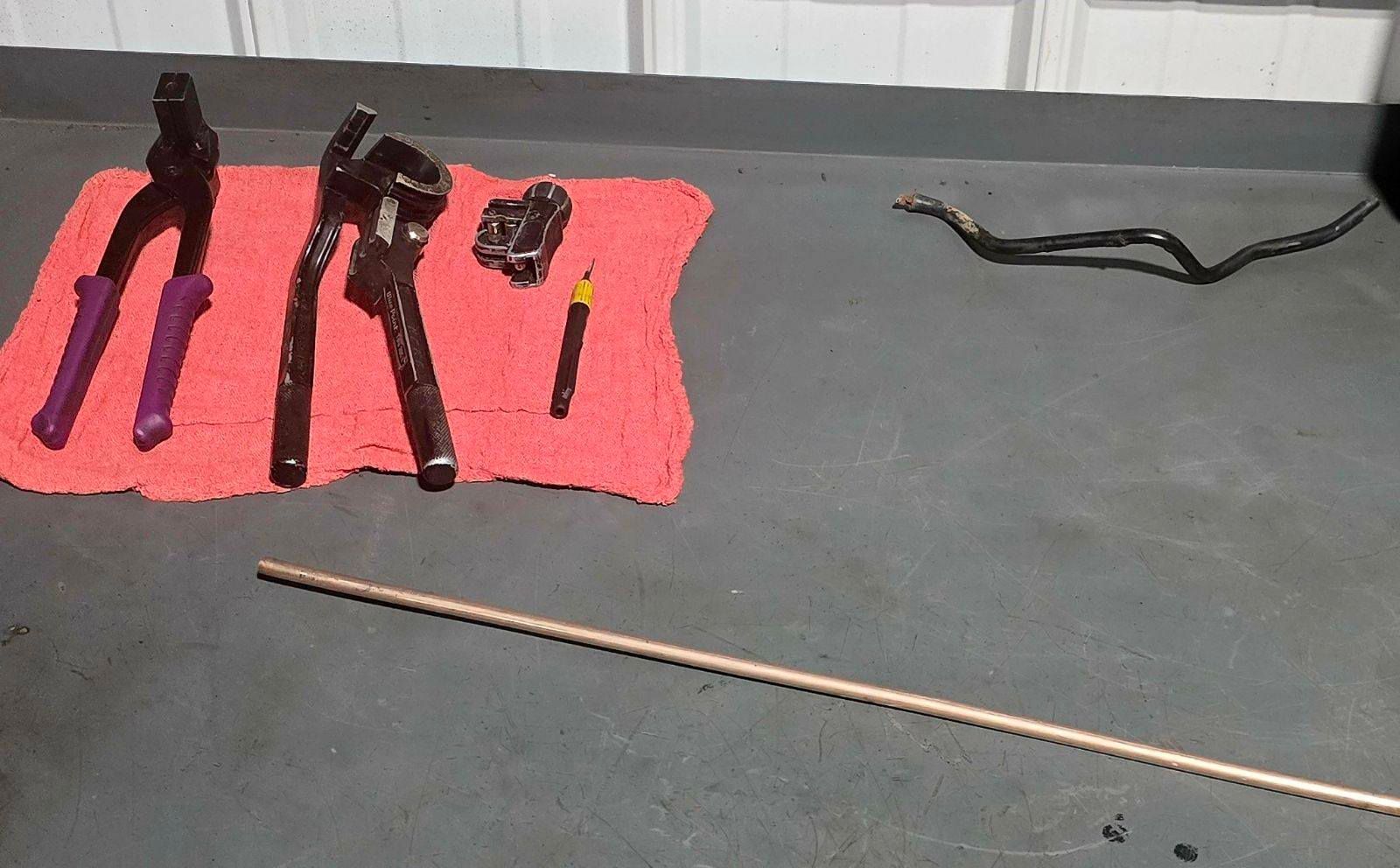 Tool parts laid out on a black table, including pliers, cutters, and a wrench on a pink cloth, with a cord nearby