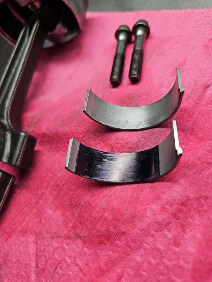 Black metal hardware parts and two curved silver/black pieces on a pink cloth.