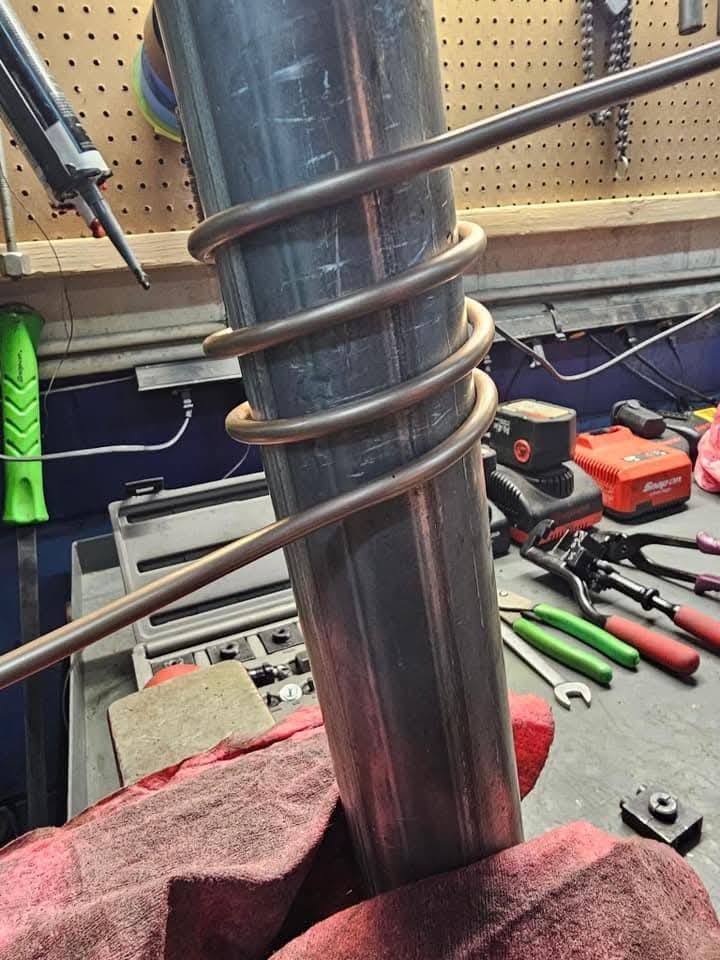 Metal pipe with a coiled spring clamp in a workshop, with tools and a red towel nearby