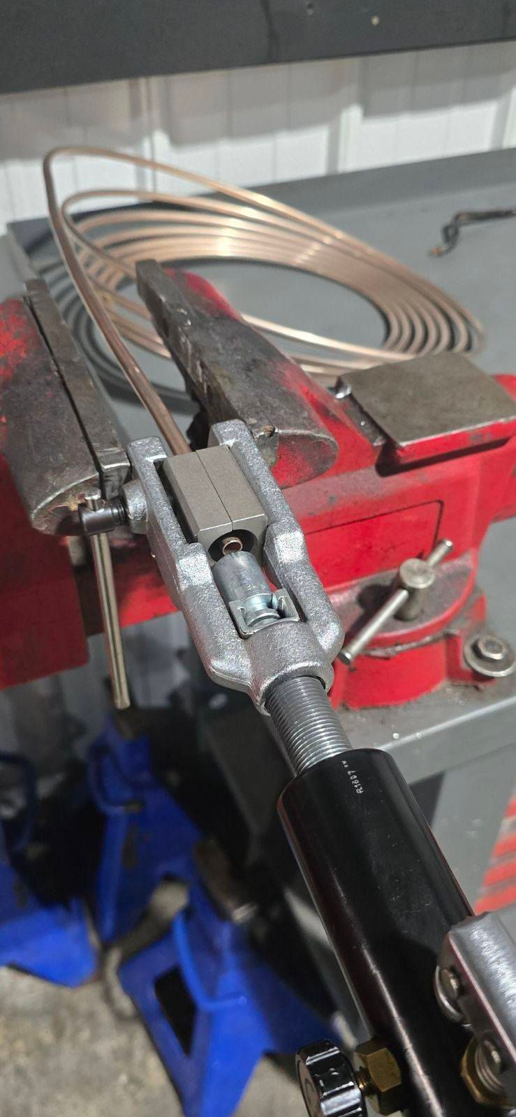 Copper tubing coiled on a red workbench vise with a black hose attached.