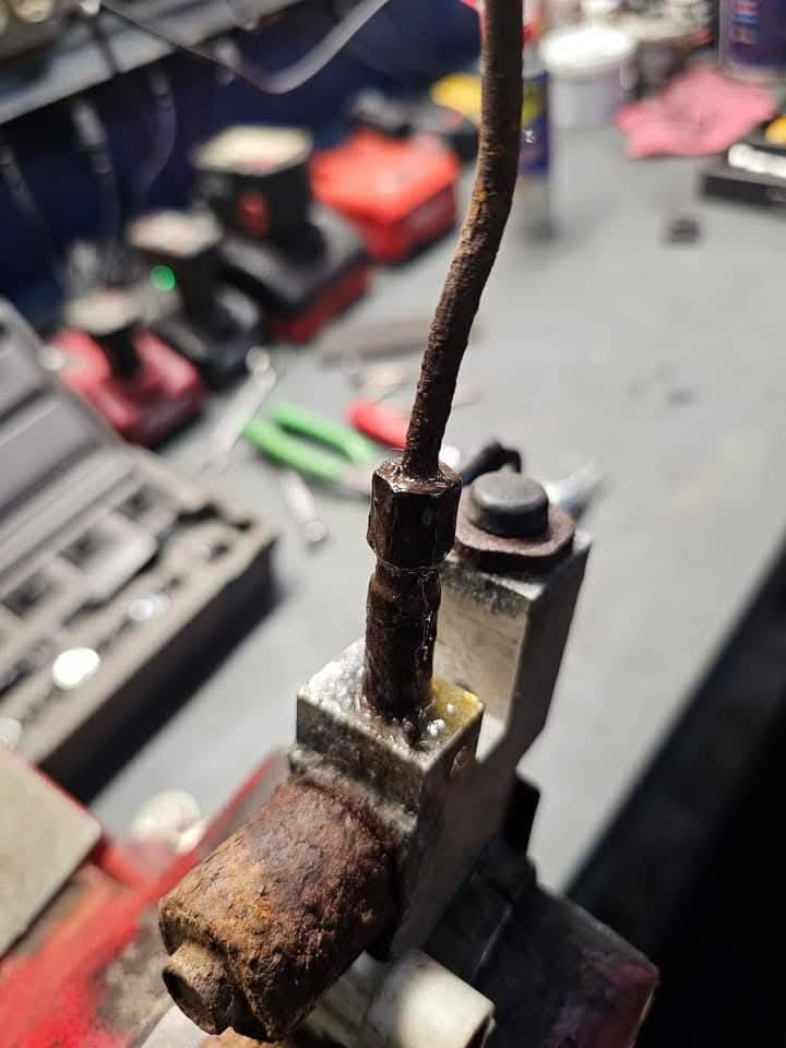 Close-up of a rusty metal tool part with a cable attached, on a workbench with blurred tools in the background