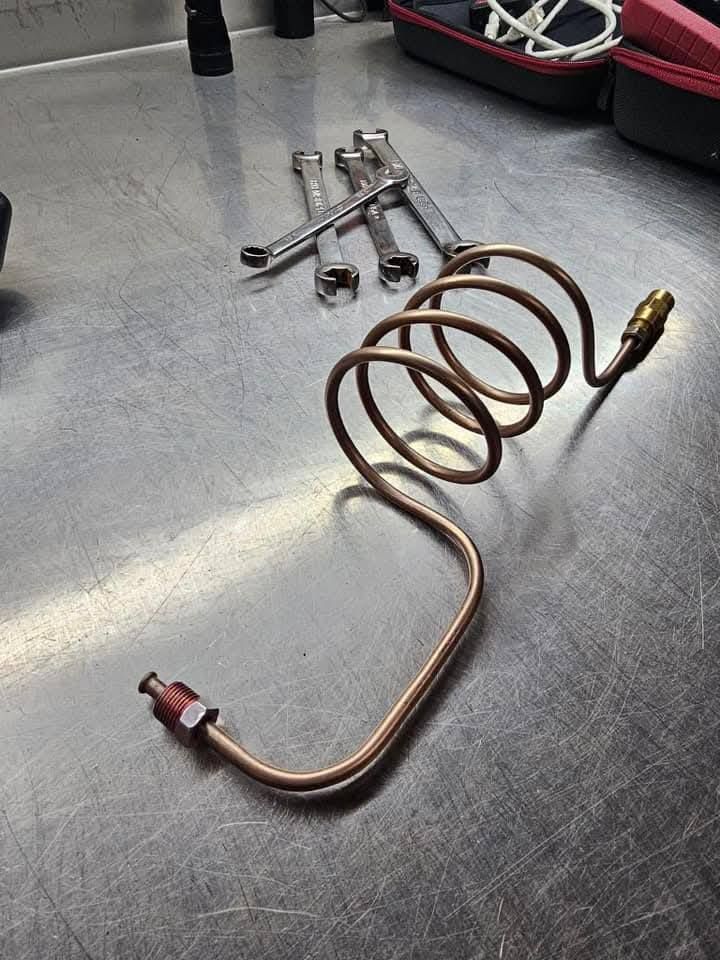 Coiled copper tube with brass fittings on a metal workbench, with small metal parts in the background