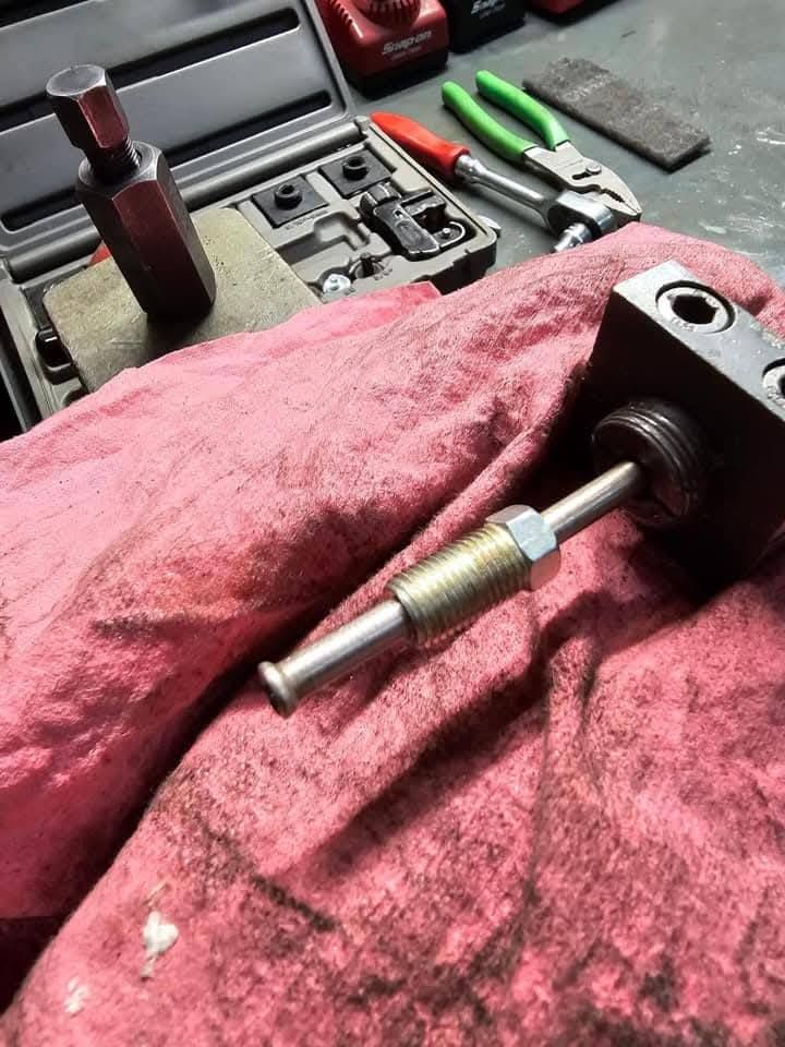 Close-up of a metal vise with a threaded rod resting on a red shop towel, tools in the background.