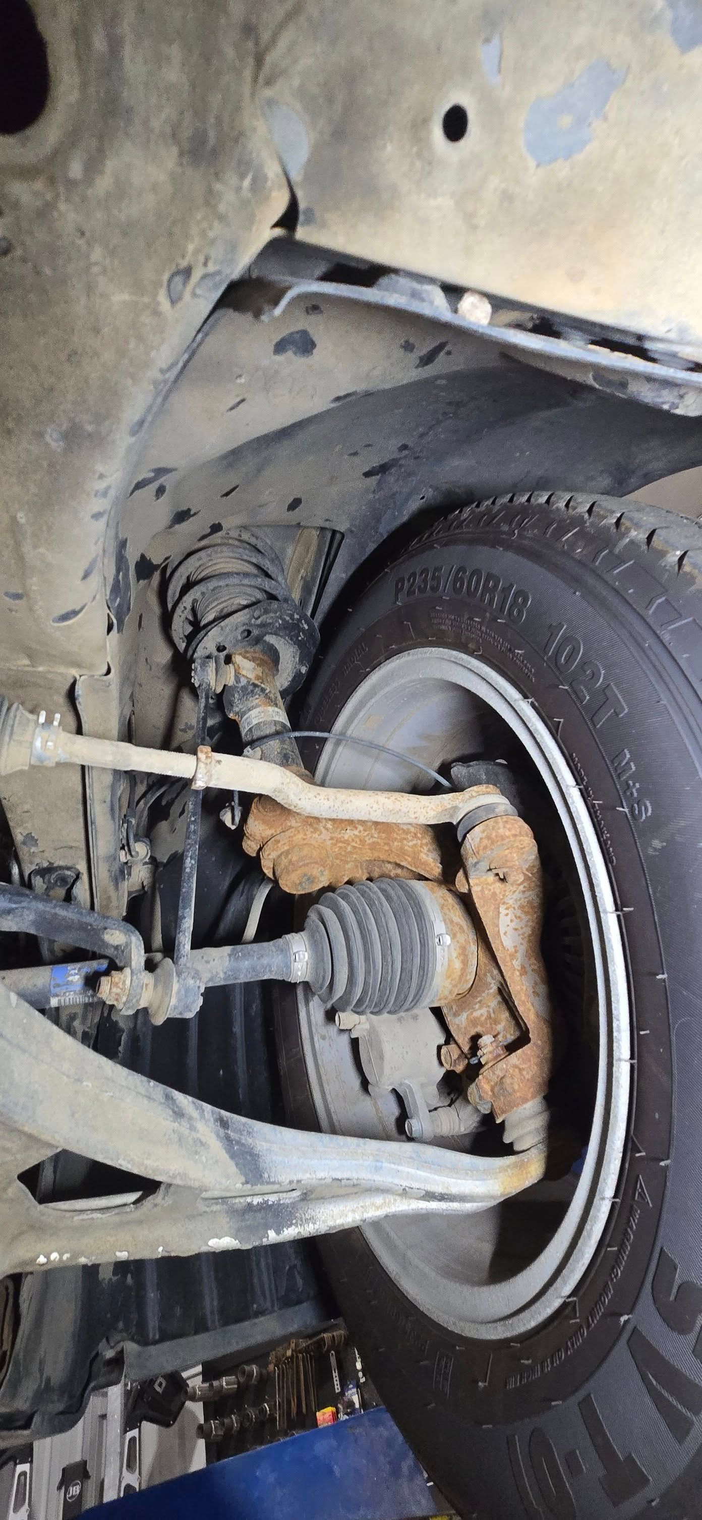 Close-up of a car’s rear wheel, suspension, and rusty brake components inside the wheel well.