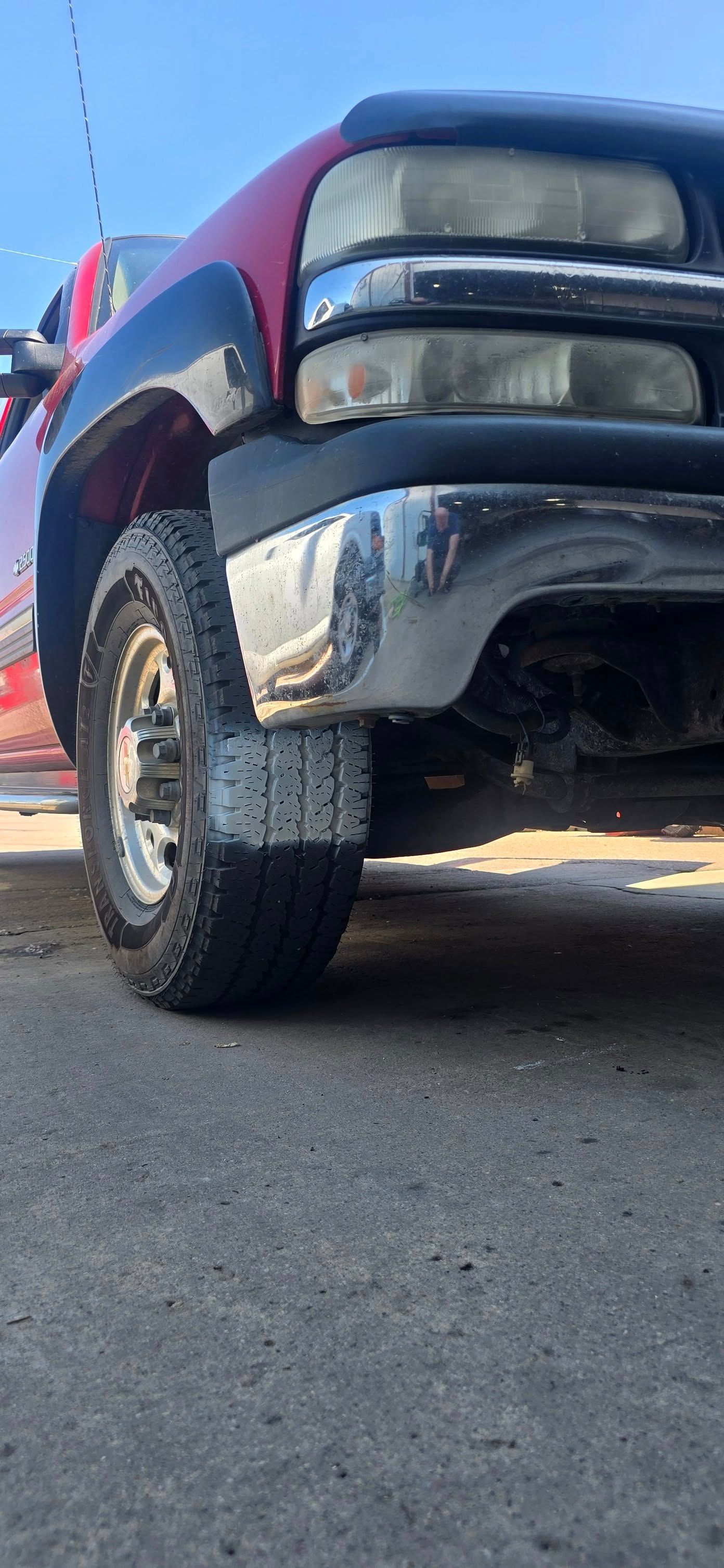 Low-angle view of a maroon pickup truck’s front bumper and wheel on pavement