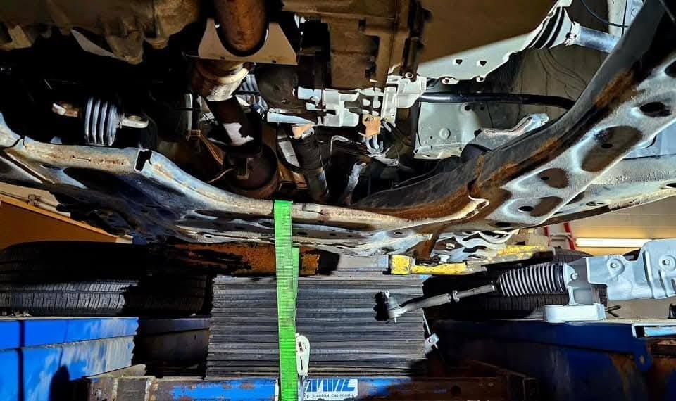 Undercarriage of a vehicle on a lift, with a green strap hanging down in a repair shop