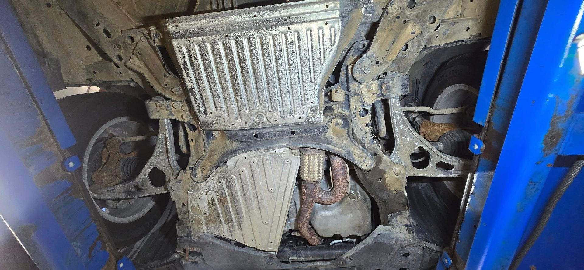 Undercarriage of a vehicle with exposed metal components and blue side panels, showing rust and wear