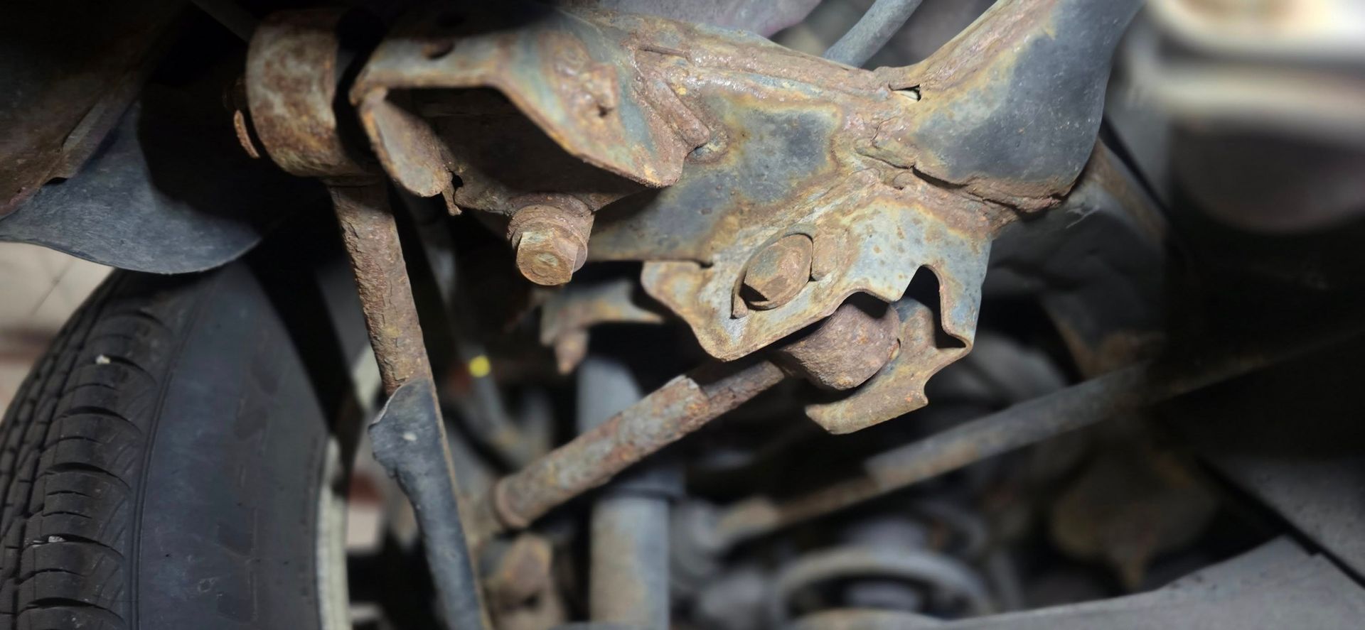 Rusty car suspension or steering joint under a vehicle, with worn metal parts and a cracked rubber boot