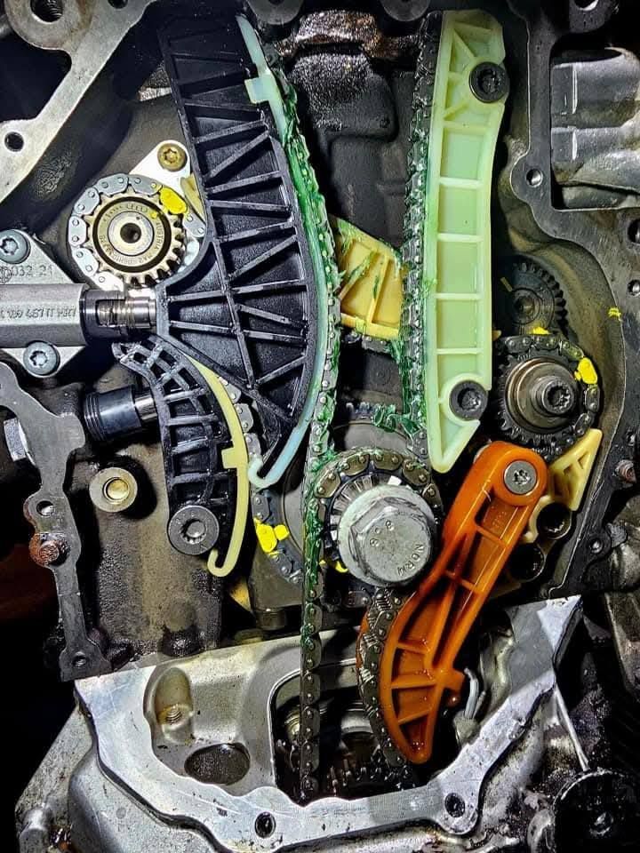 Close-up of an engine timing chain assembly with green, orange, and black plastic guides and metal gears.