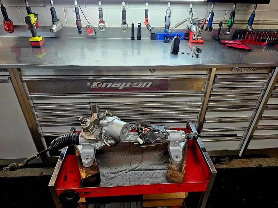 Automotive transmission assembly on a red stand in a workshop, with a Snap-on tool chest and tools behind it