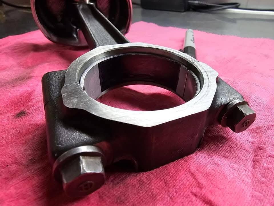 Metal connecting rod end with bearing cap and bolts on a pink cloth background