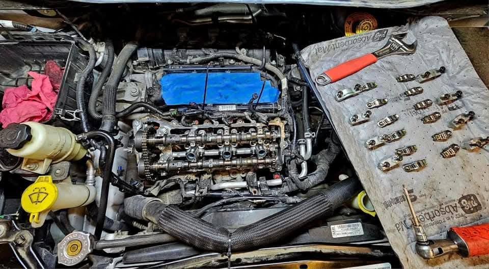 Car engine bay with exposed cylinder head and a blue cover, tools laid out on the right.