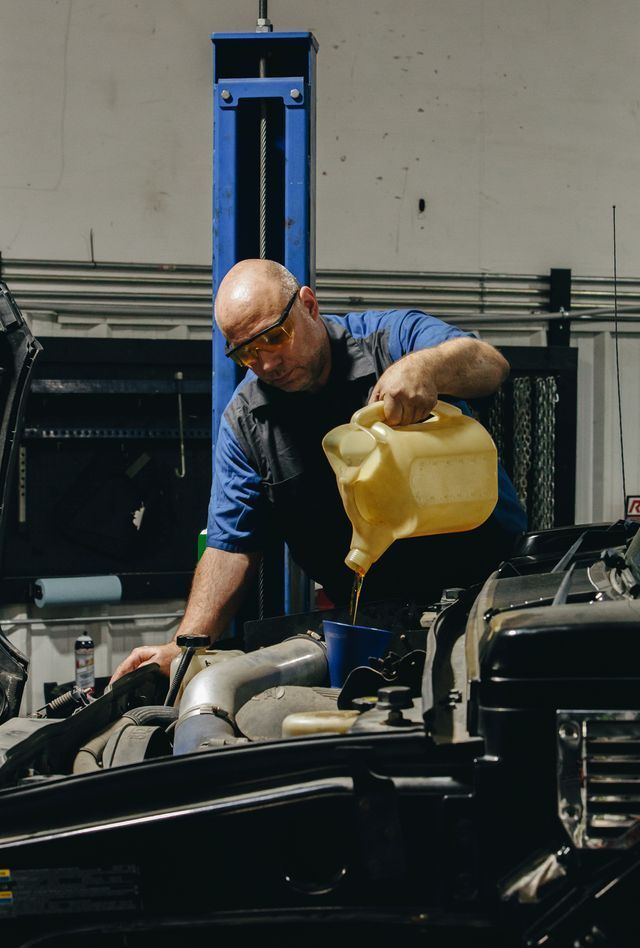 Mechanic pouring oil into a car engine in a garage