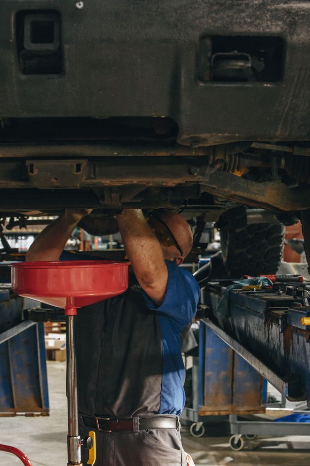 Mechanic working under a raised car in a repair shop, using a red oil drain pan