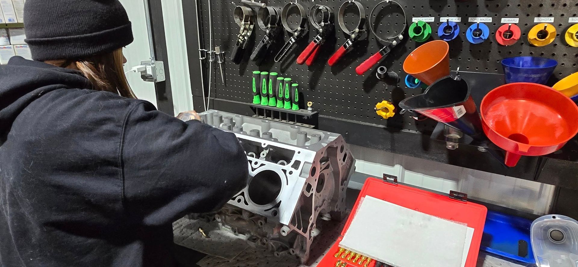 Person in a black jacket inspecting a metal part beside a control panel with colorful knobs and funnels.