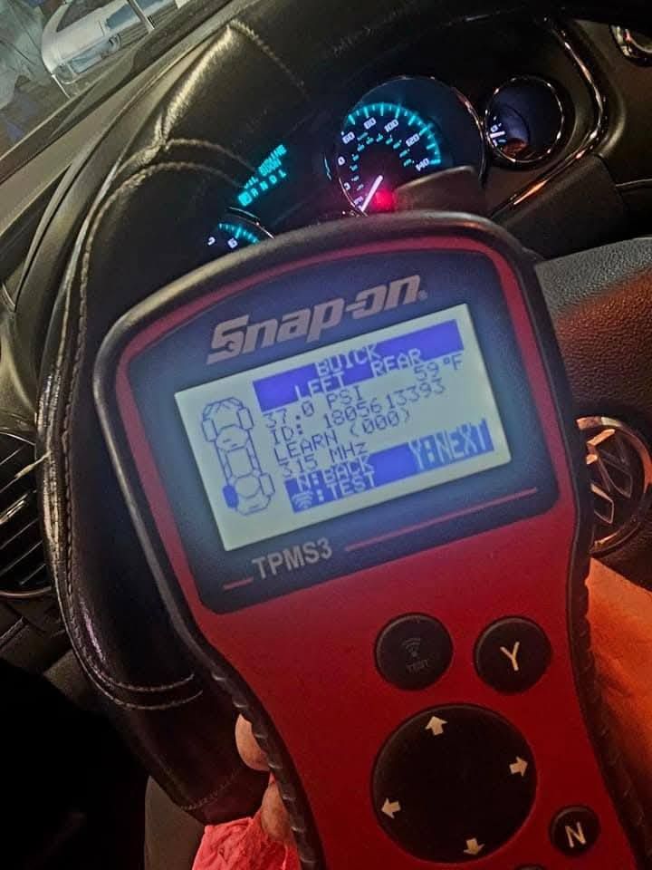 Snap-on TPMS tool in a car, showing a blue backlit screen and steering wheel dashboard behind it