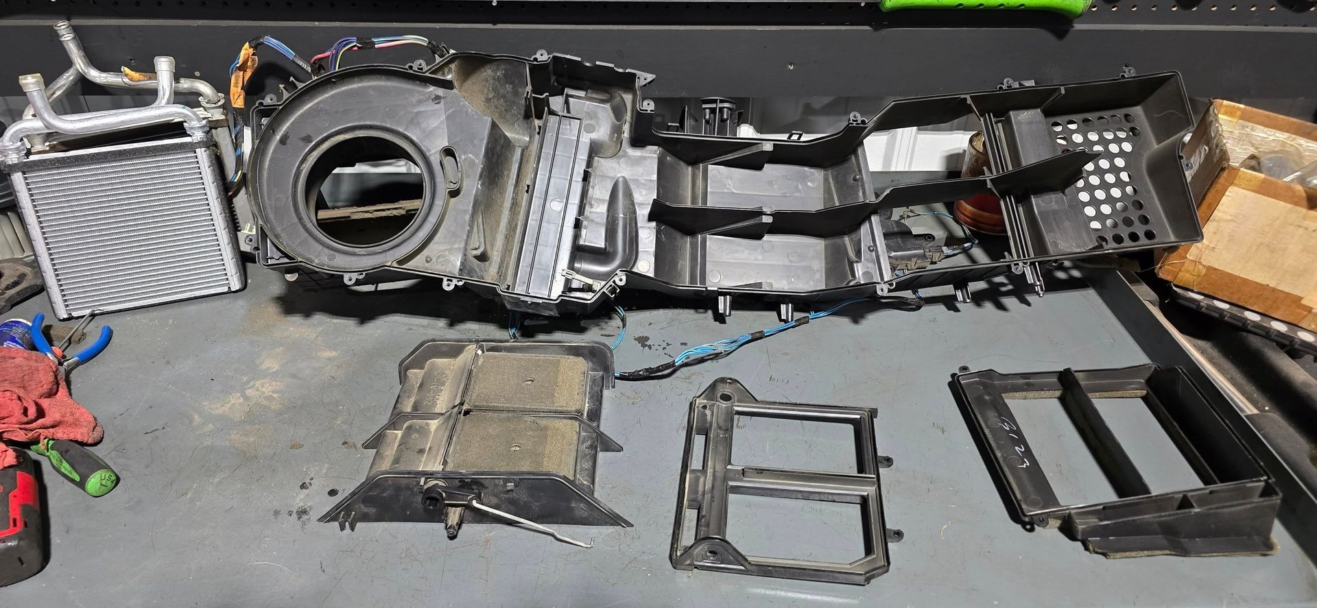 Scattered disassembled car dashboard parts and trim pieces on a gray workbench, including a circular vent housing.