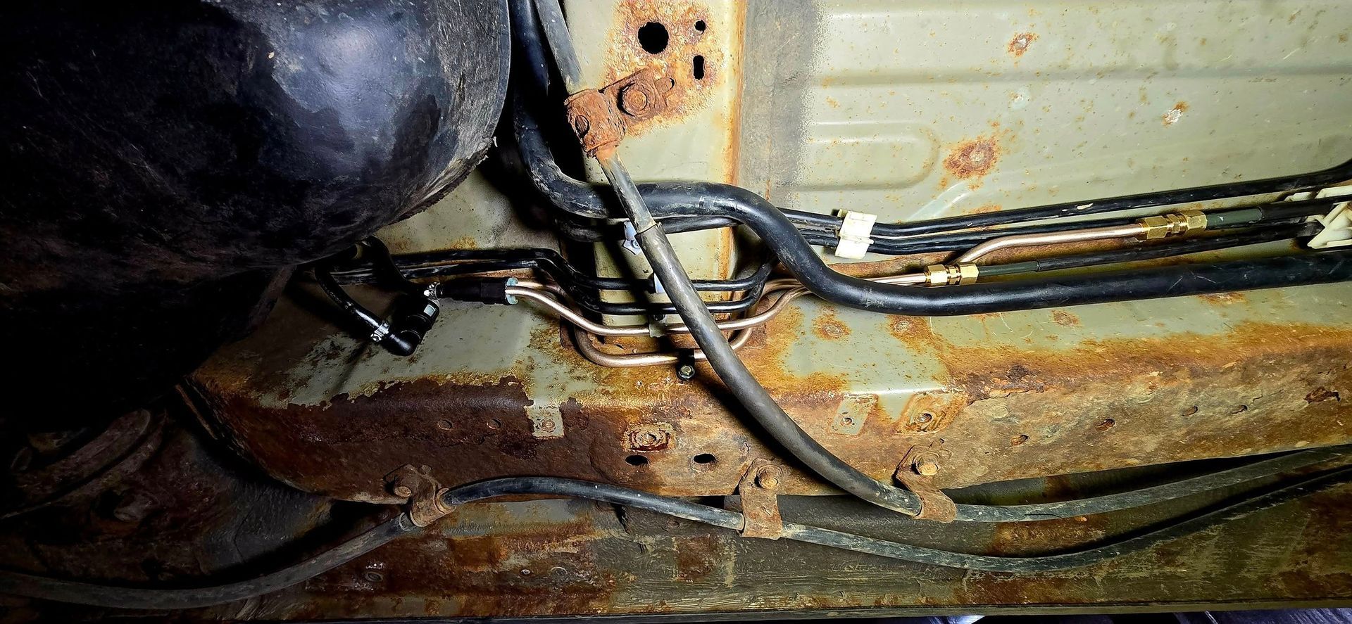 Rusty metal undercarriage with wires and hoses attached, showing corrosion and grime