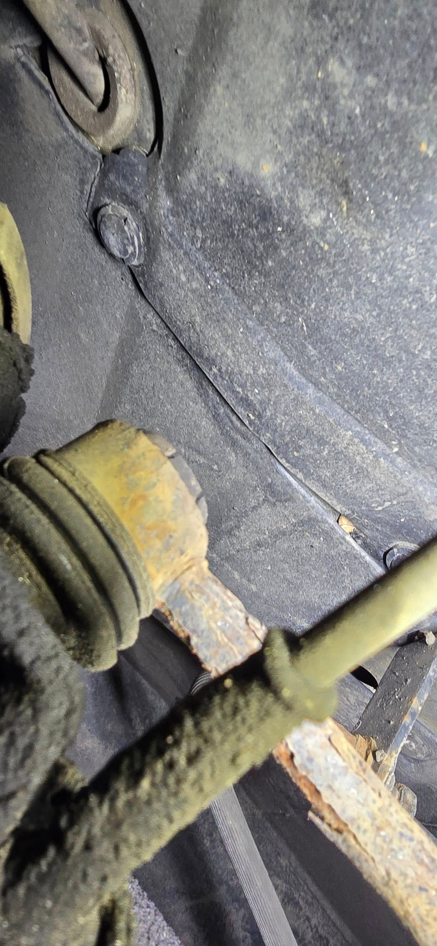 Close-up of a dusty mechanical belt and pulley assembly with wires and a rusted metal frame.
