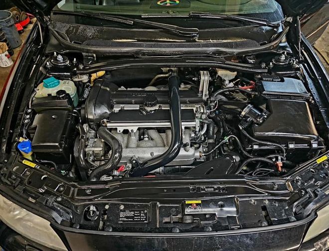 Open car hood showing a clean engine bay with black components and hoses.