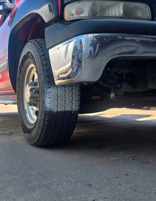 Close-up of a black vehicle’s front tire and bumper parked on pavement in sunlight