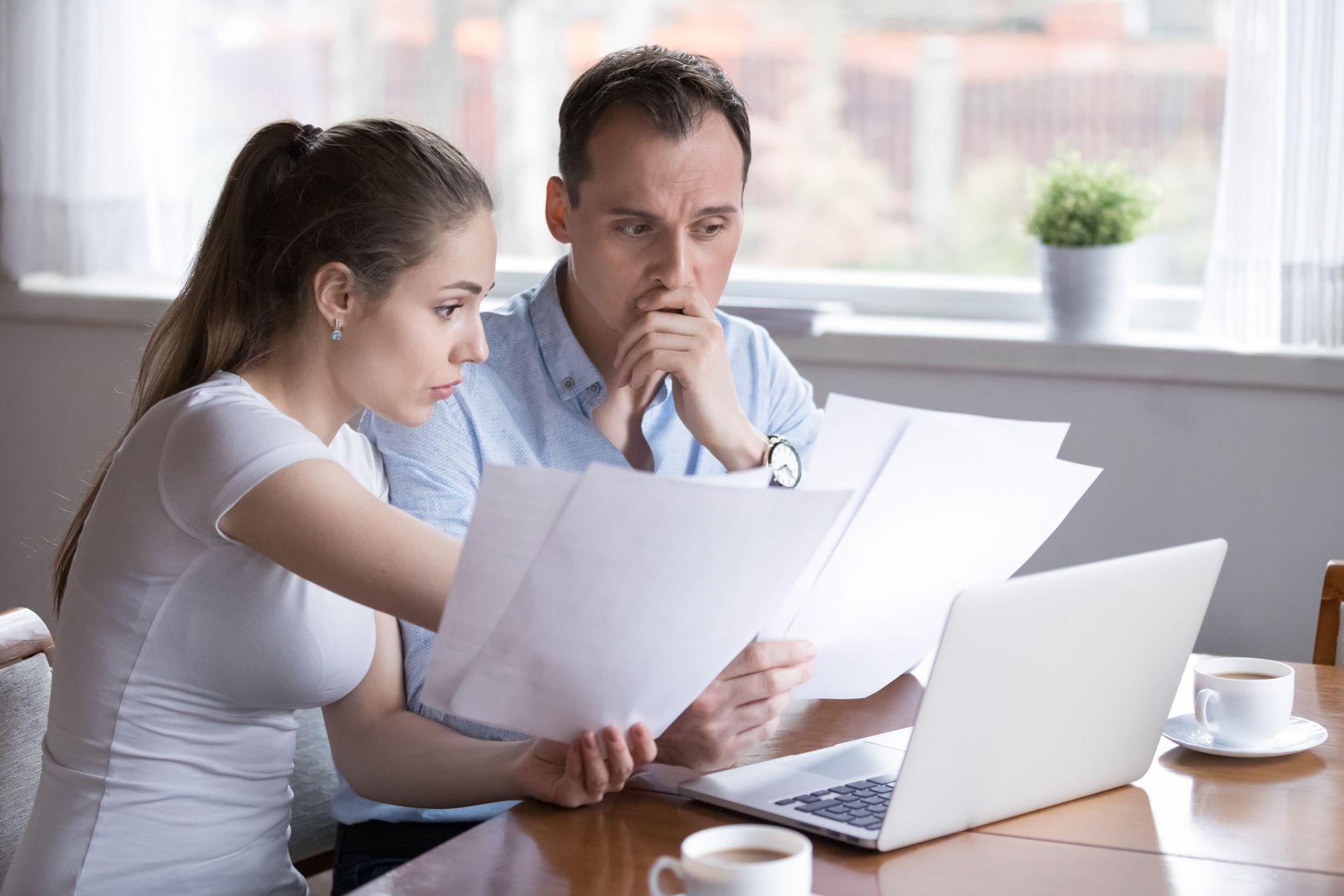 A man and a woman are sitting at a table looking at papers and a laptop.