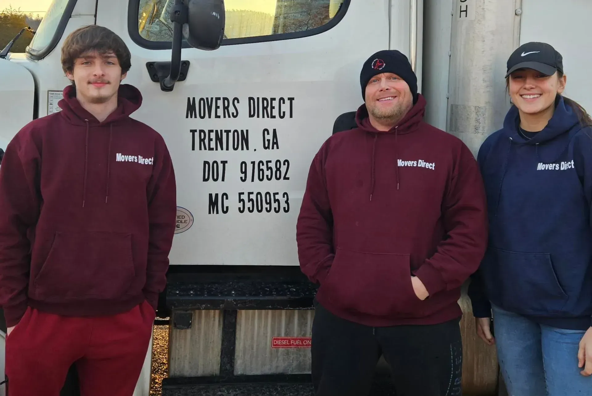 Three people wearing maroon hoodies stand in front of a truck labeled 