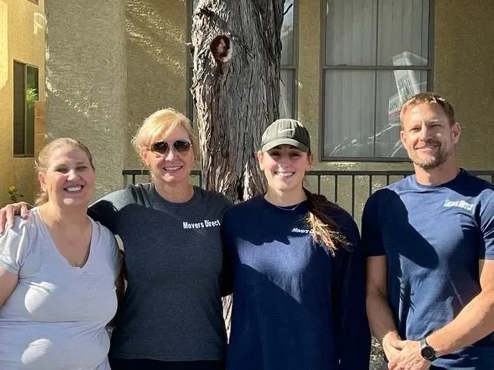 Four people in front of a building and tree: two women and two men. All smiling, wearing casual clothing.