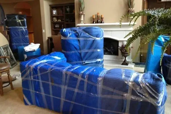 Furniture wrapped in blue moving blankets and tape, inside a home near a fireplace.