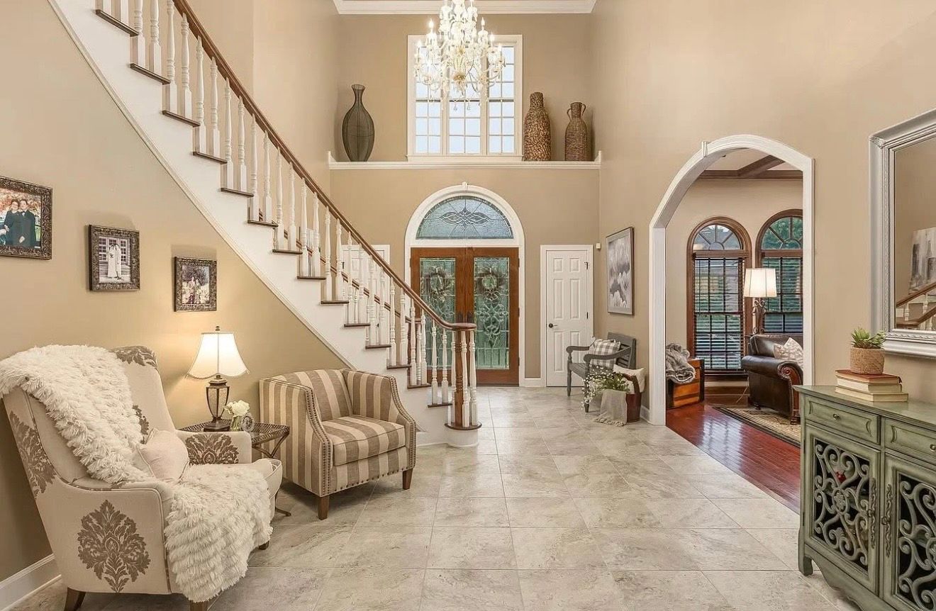 Spacious foyer with staircase, patterned chairs, and a detailed front door.