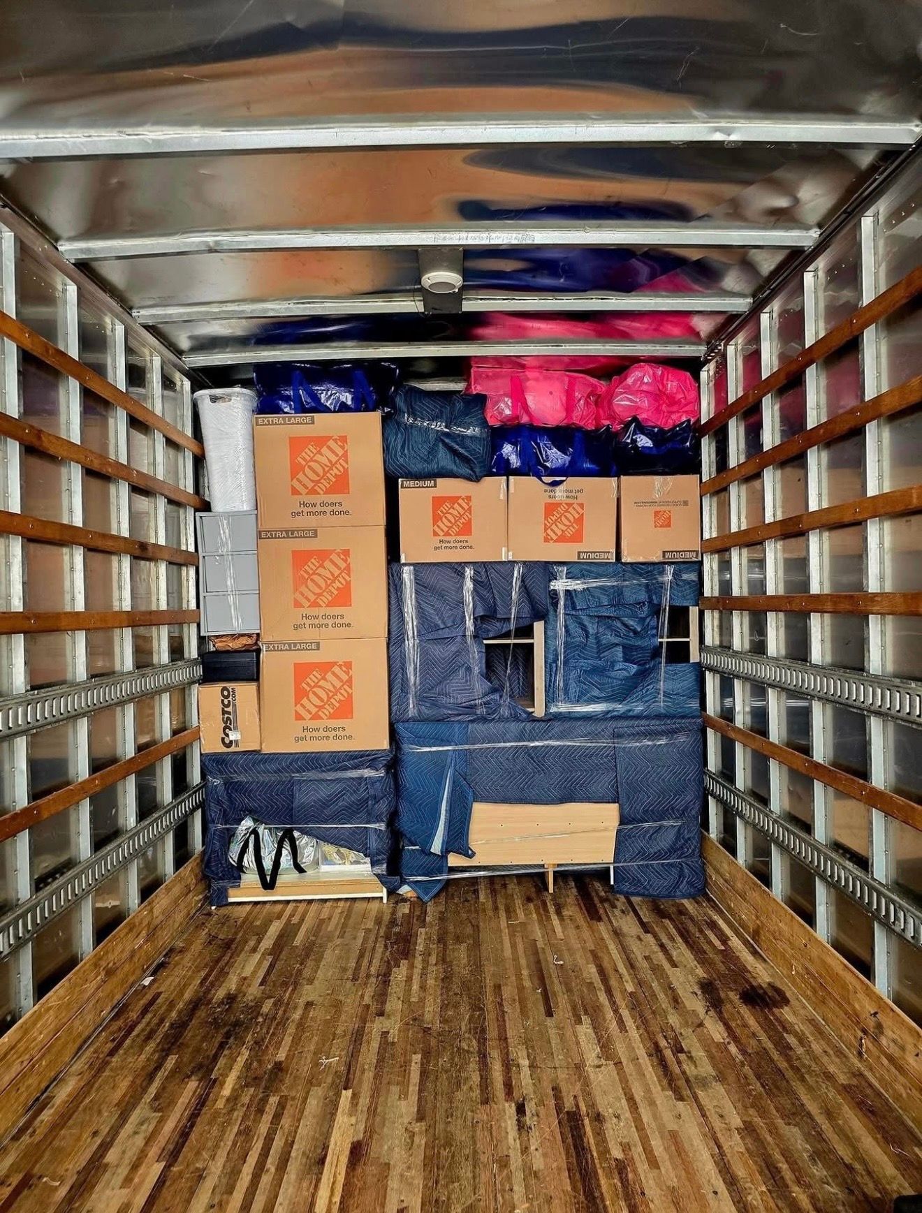 Interior of a moving truck packed with boxes and furniture wrapped in blue plastic, ready for transport.