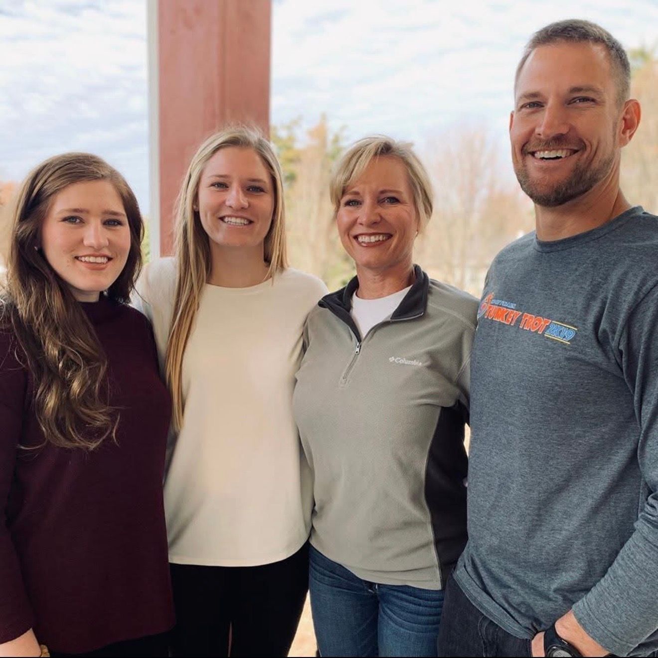 Four people smiling outdoors; two women, and two men; neutral expressions.