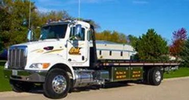 White flatbed tow truck parked on the street with a casket loaded on the bed.