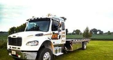 White tow truck parked on a grassy field, with farm buildings in the background.