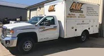 White AM Towing truck with a service body parked outdoors.