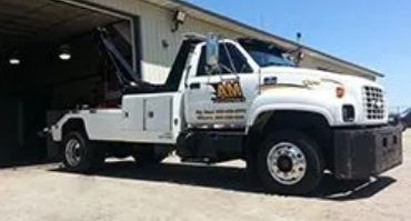White tow truck parked in front of a building; it has black crane and logo.