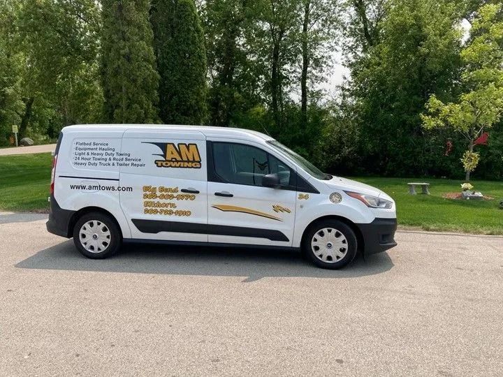 White AM Van, parked on asphalt; business logo on side, with trees in the background.