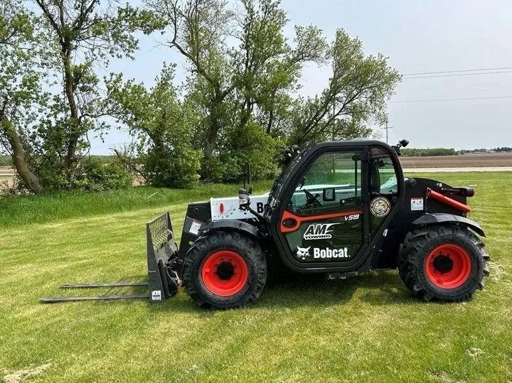 Black Bobcat telehandler with orange wheels and forks on green grass.