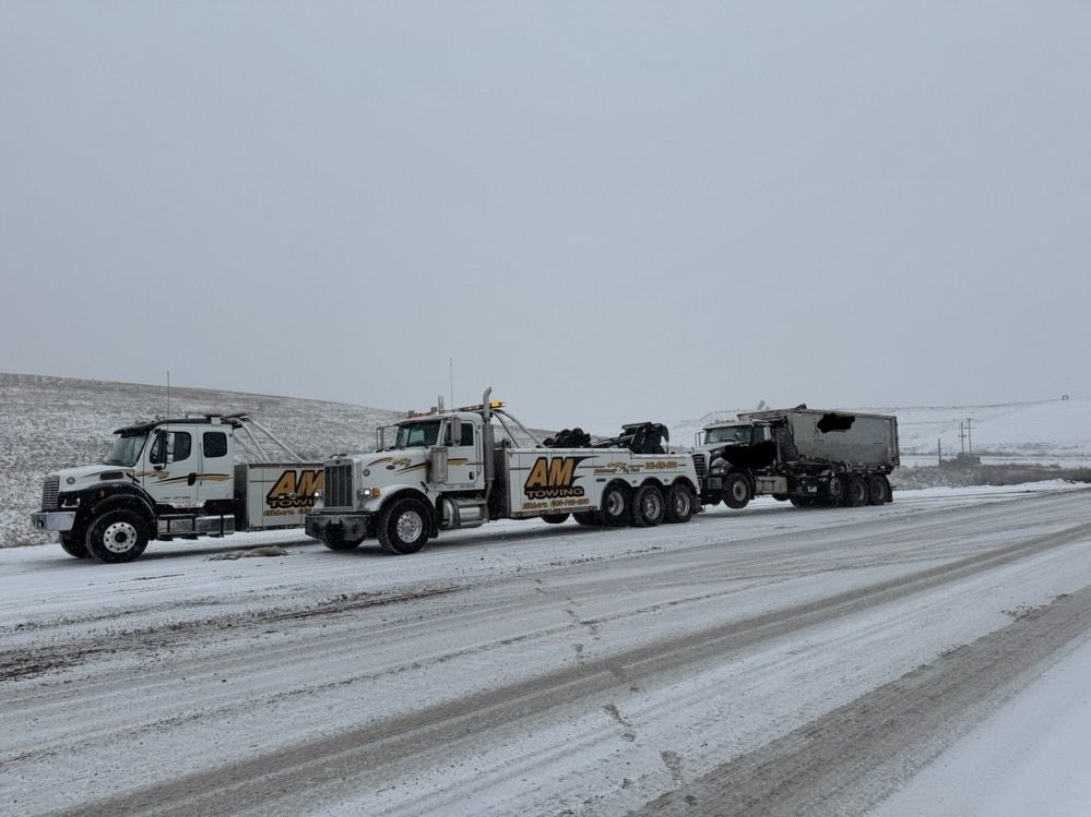 Tow trucks towing a disabled semi-truck on a snow-covered road.