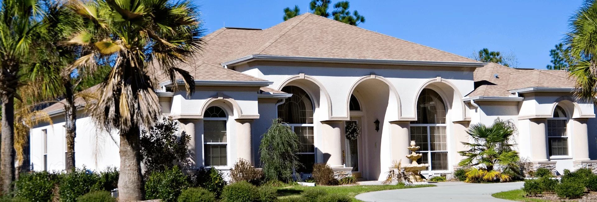 Single-story beige stucco house with arched windows and a palm tree in the front yard