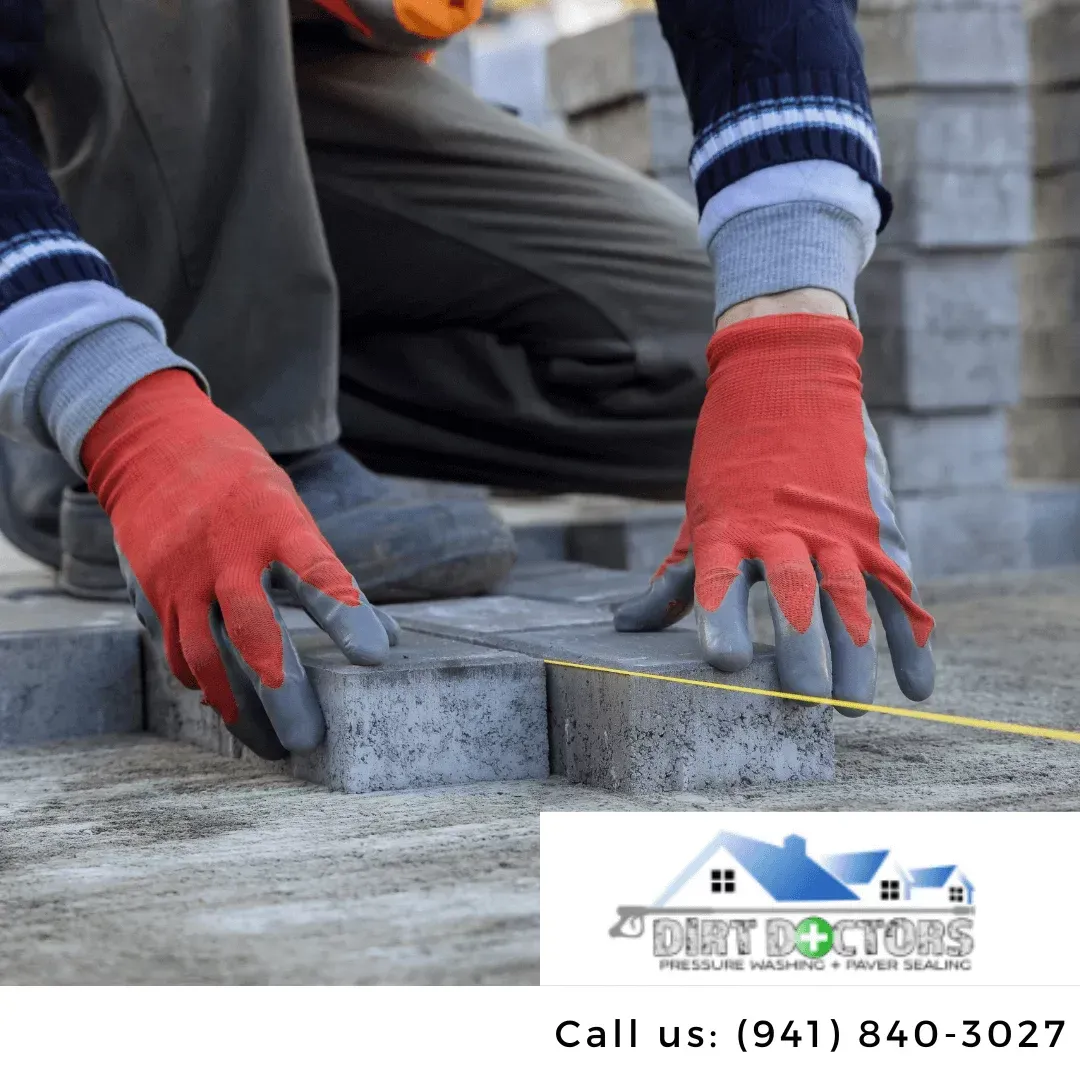 Worker in red gloves laying gray stone pavers with a tape measure on a construction site