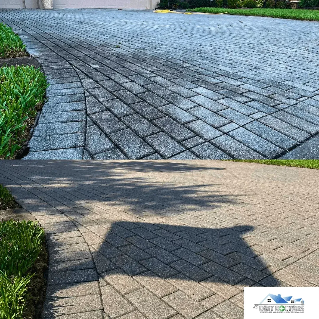 Interlocking gray paver driveway with a concrete apron and green grass borders in sunlight