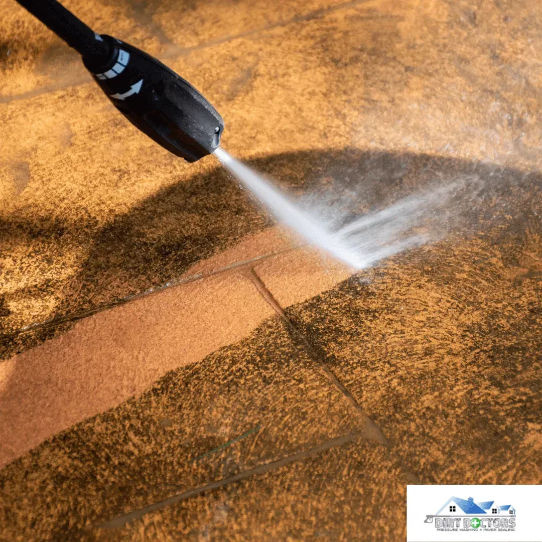 Pressure washer spraying water across a tan surface, cleaning a bright streak on the ground