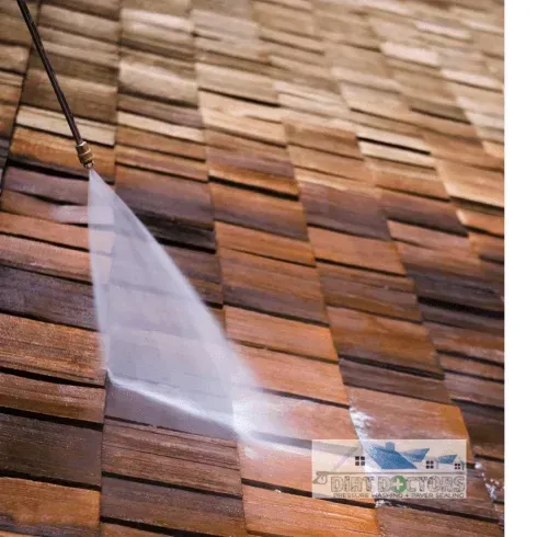 Water spraying from a hose onto a wooden shingle wall during cleaning