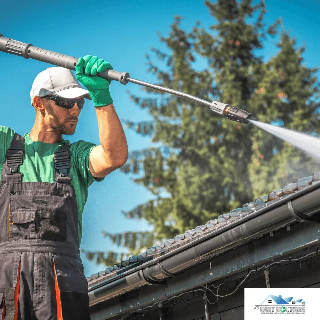 Worker pressure-washing a roof with a long spray wand on a sunny day