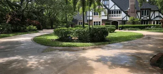 Curved driveway around a landscaped roundabout in front of a Tudor-style house with trees and lawns